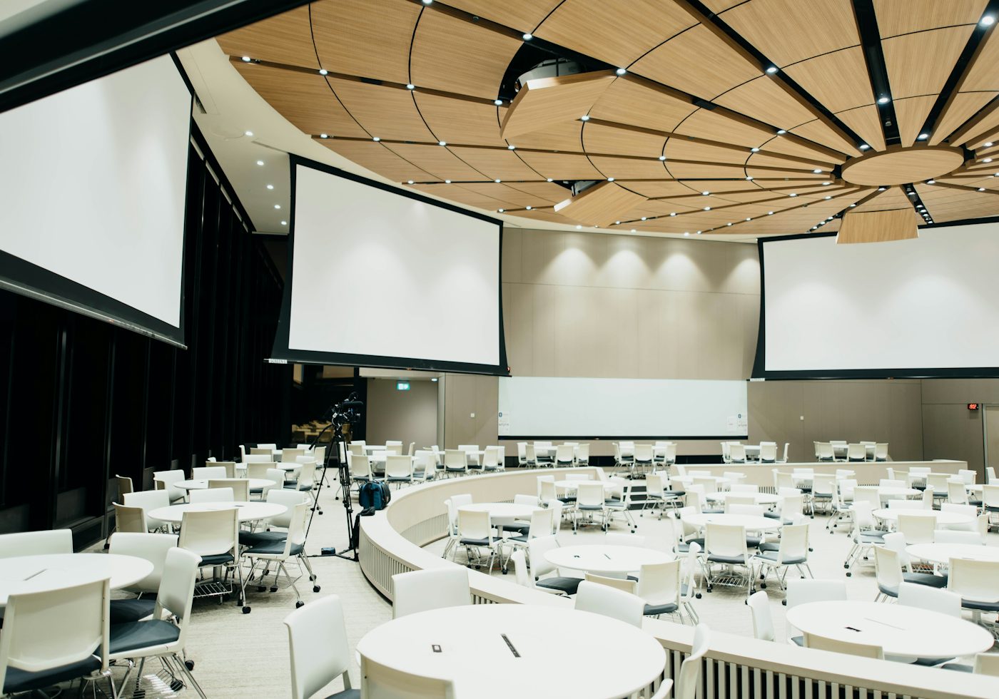 A bright hall set with round tables and projection screens, ready for a gathering.